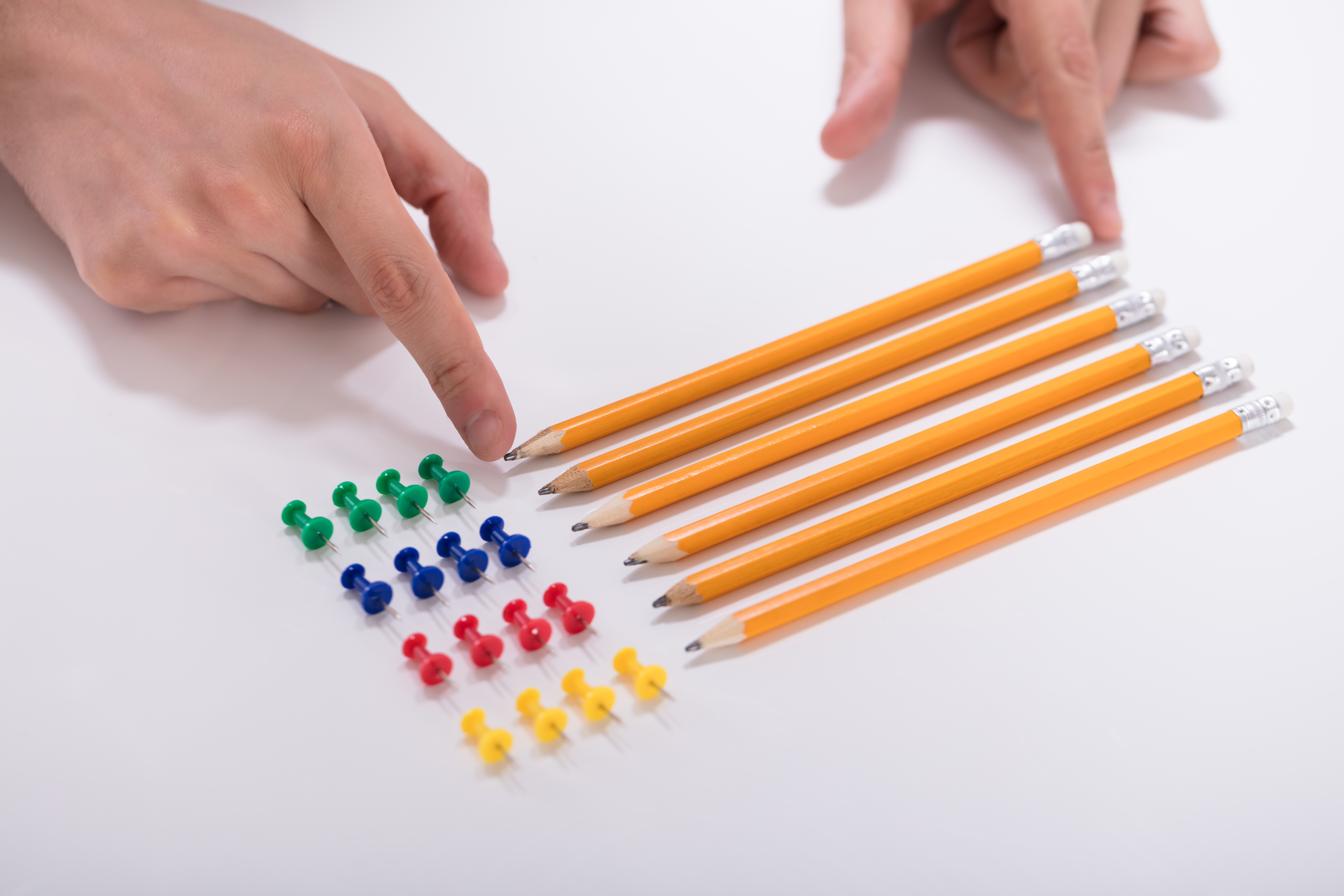 Person’s Hand Arranging Pencils And Multi Colored Pushpins