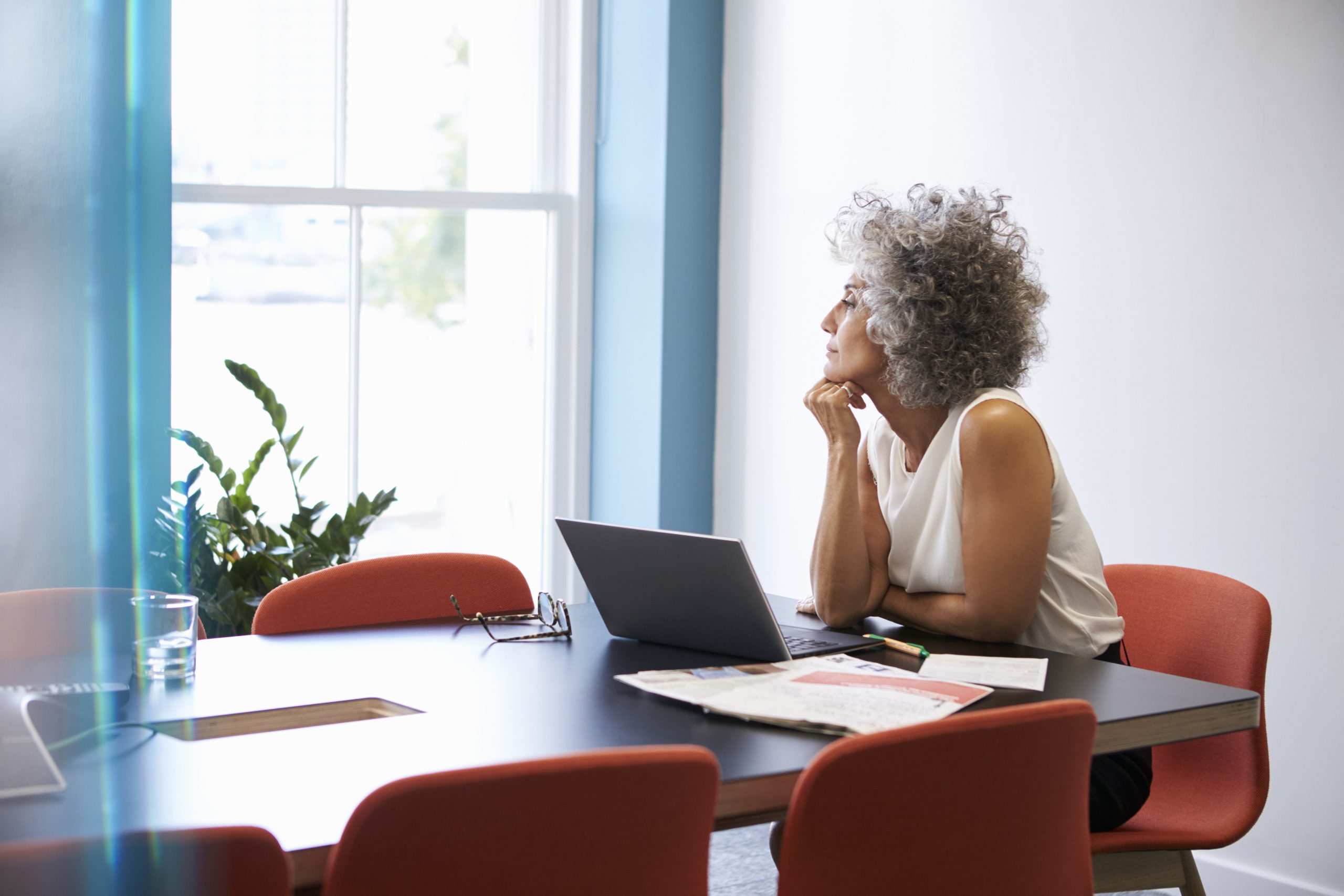 Middle aged woman looking out of the window in the boardroom First things first